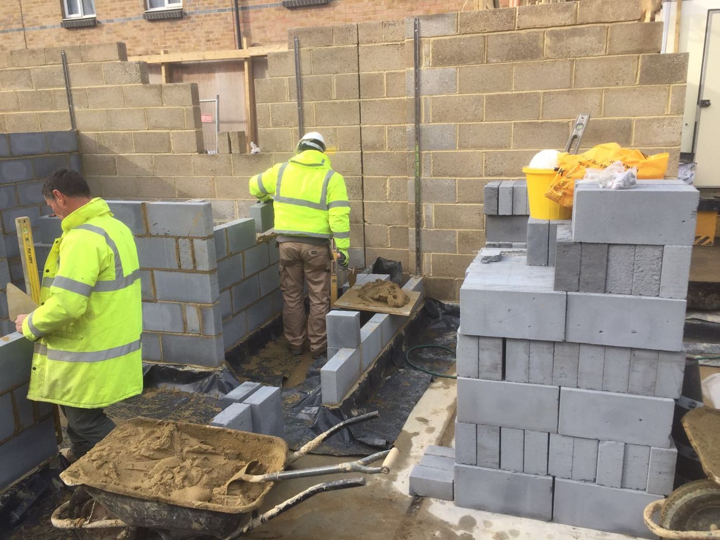 Two bricklayers in hi-vis building blockwork walls